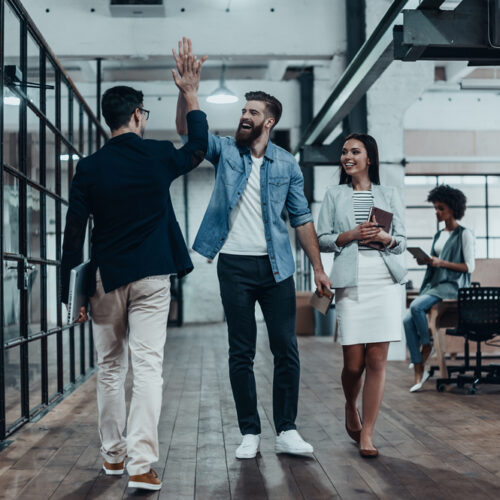 High-five!  Full length of two cheerful young business people giving high-five while their colleague looking at them and smiling